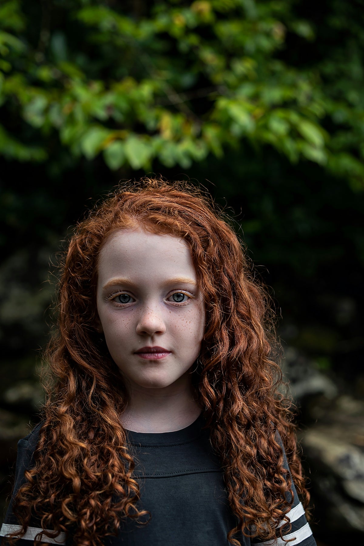 A child with long curly red hair and freckles in a black shirt Image
