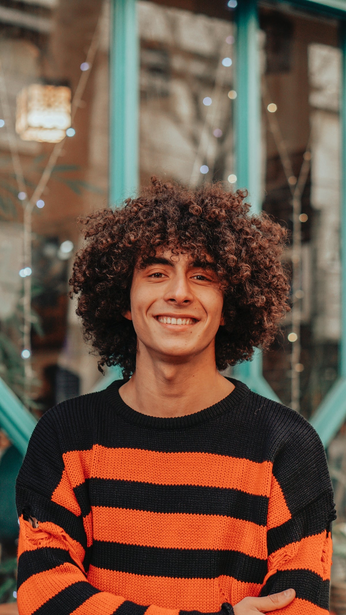 a man with curly hair wearing an orange and black striped sweater Image