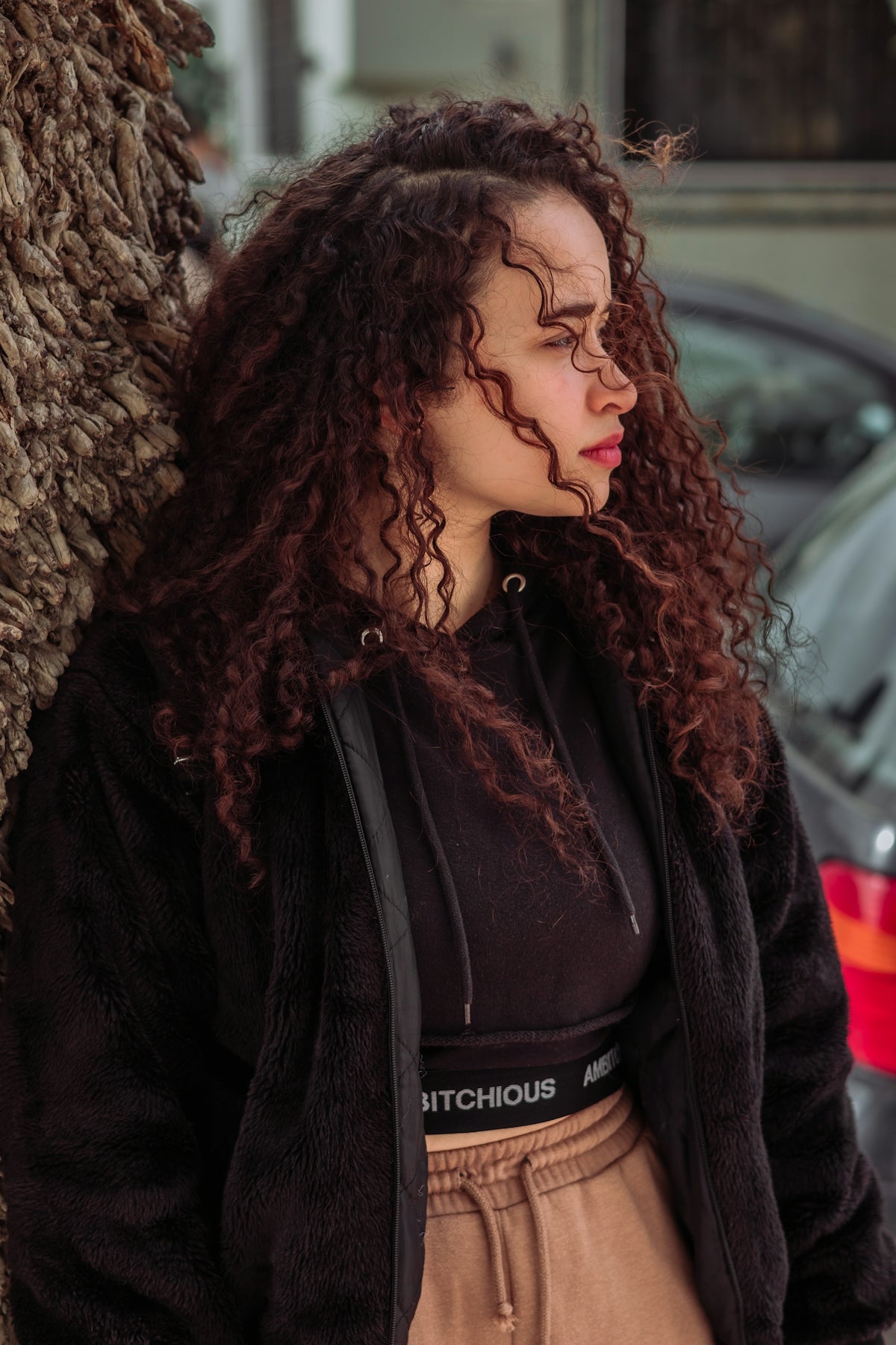 a woman with curly hair standing next to a tree